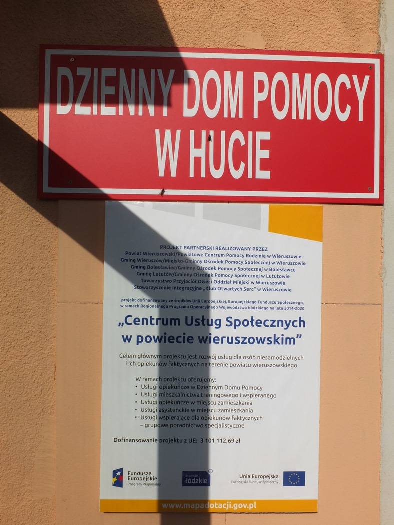 tablica na scianie budynku Dzienny Dom Pomocy, pod tablicą plakat informujący o projekcie, w ramach, którego powstał Dom