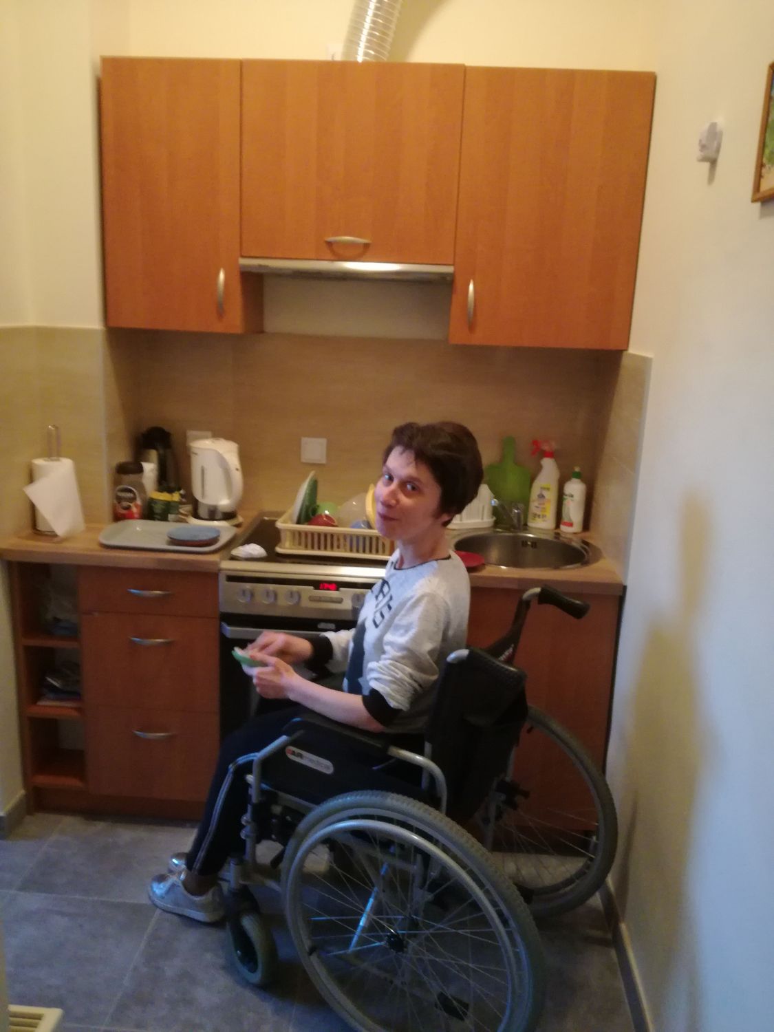 Mieszkanka mieszkań wspomaganych na wózku inwalidzkim podczas wycierania naczyń w aneksie kuchennym