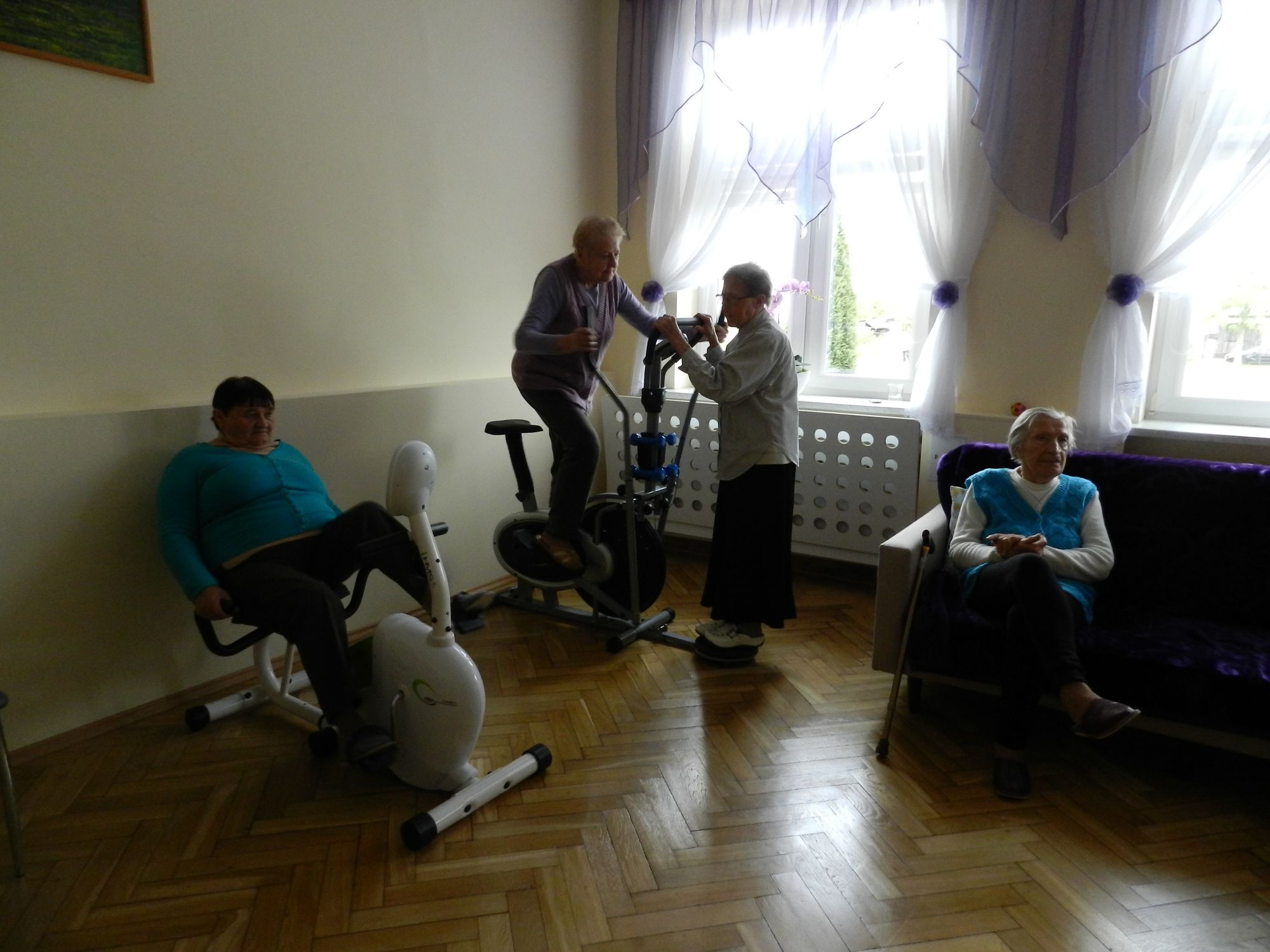 2 uczestników w sali rehabilitacji, 1 osoba ćwiczy na rowerku, 2 osoba ćwiczy na orbitreku